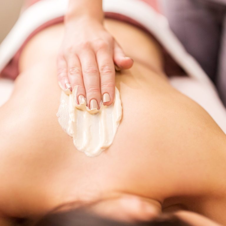 Therapist applying an exfoliating body scrub to the back